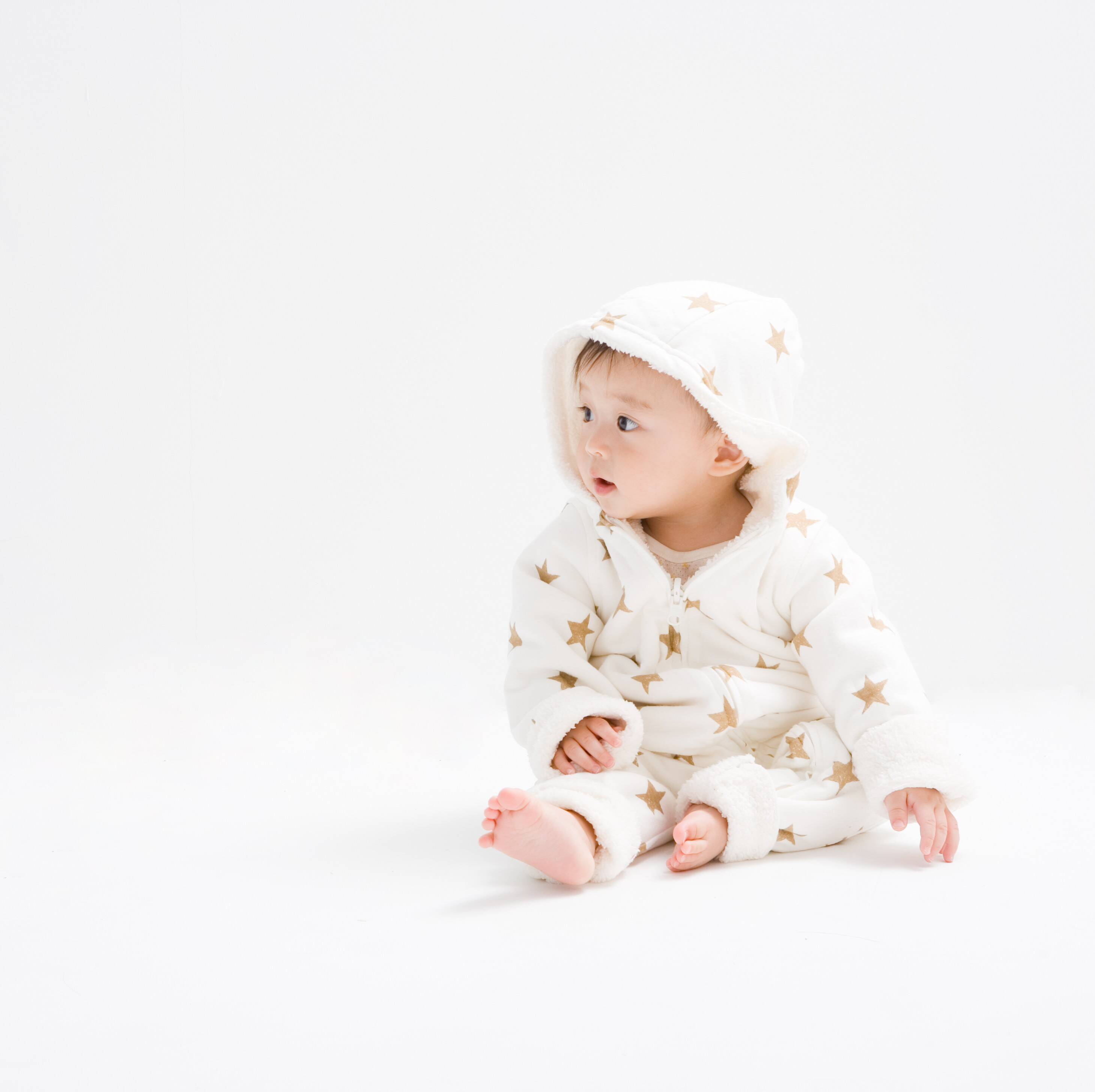 白色の背景に赤ちゃんが座りながら横を見つめています。